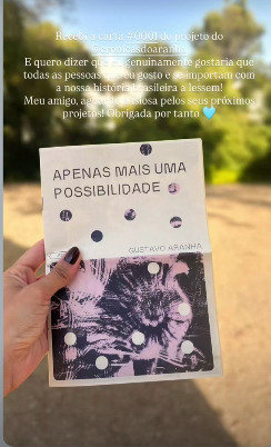 Mão segurando o libreto 'Apenas mais uma possibilidade' ao ar livre